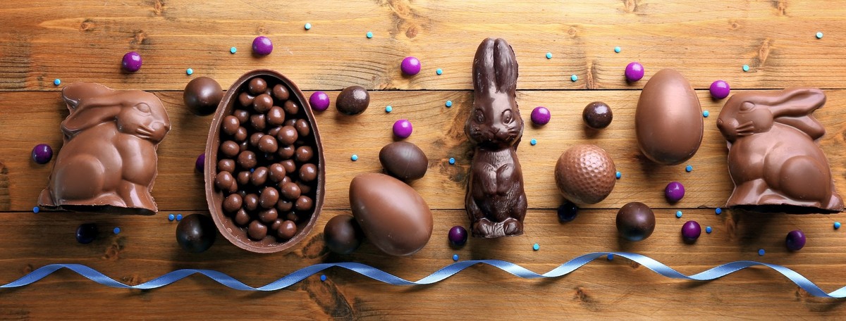 Easter background greeting card with holiday traditional confectionery, Easter egg hunt fun concept. Chocolate bunny, chocolate and candy Easter eggs on wooden background