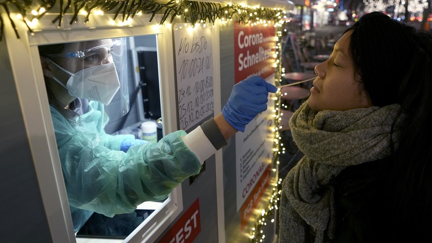 A test center employee performs a coronavirus test as she stands in the 'Kurfuerstendamm (Ku'damm)' shopping road in Berlin, Germany, Tuesday, Dec. 21, 2021. Germany has announced new restrictions aim ...