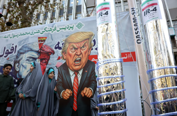 Iraner gehen in Teheran an einer Karikatur von Donald Trump vorbei.