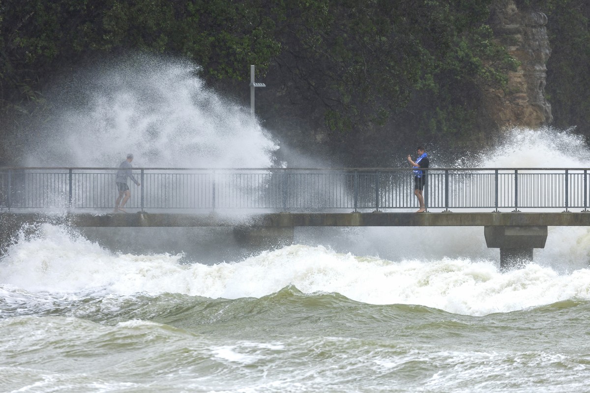 People watch as waves crash against the cliffs at an Auckland beach as a cyclone hits the upper parts of New Zealand, Sunday, Feb. 12, 2023. New Zealand's national carrier has canceled dozens of  ...