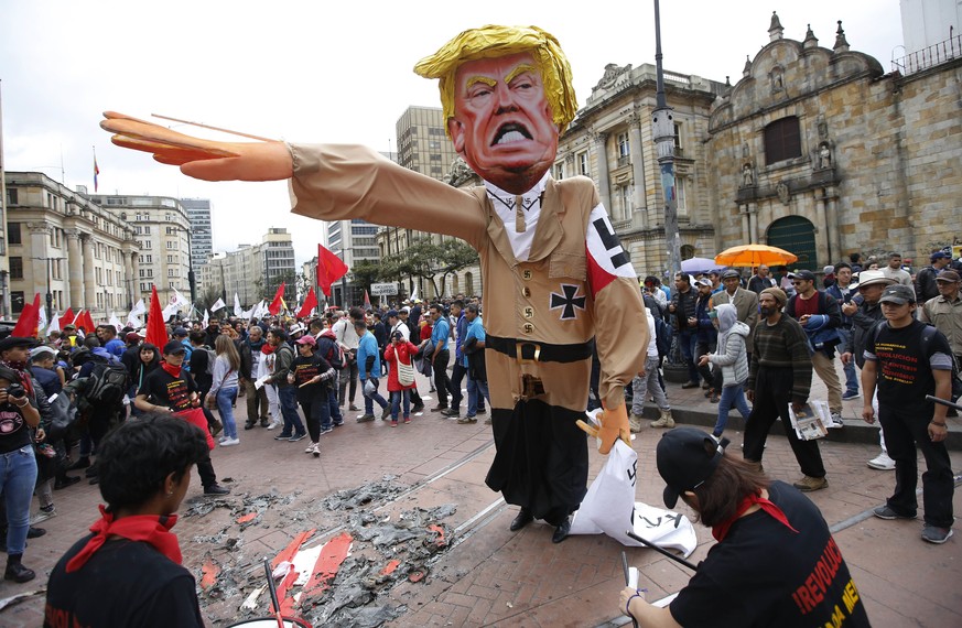 In this May 1, 2018 photo, protesters prepare to set fire to an effigy depicting U.S. President Donald Trump dressed in a Nazi uniform, during a demonstration marking May Day to honor workers, in Bogo ...