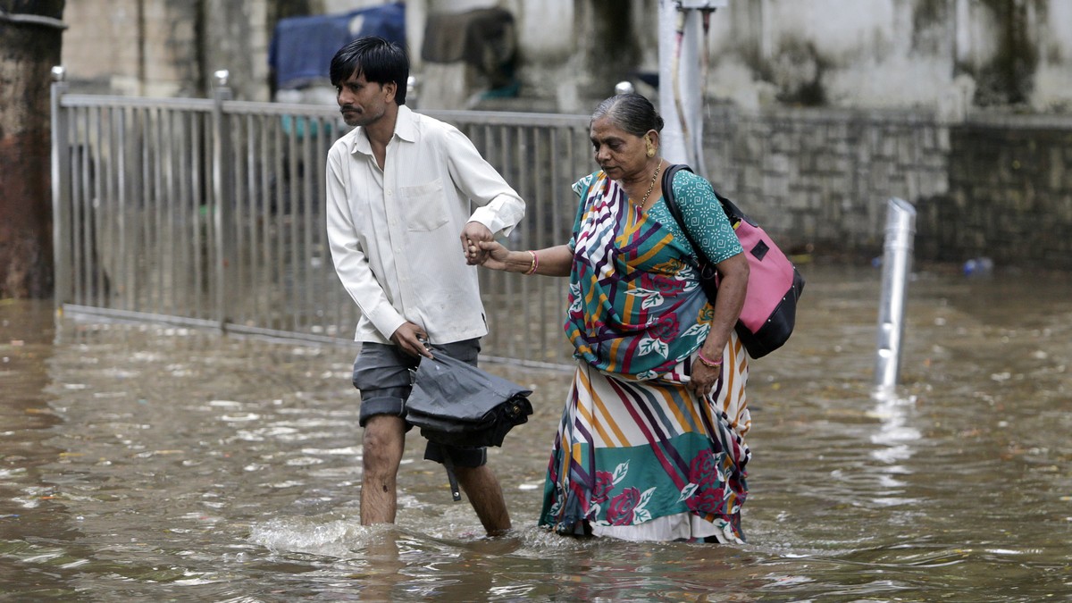 A man holds the hand of an elderly woman and helps her past a waterlogged street in Mumbai, India, Thursday, June 7, 2018. India's commercial capital has been hit by heavy rainfall, disrupting no ...
