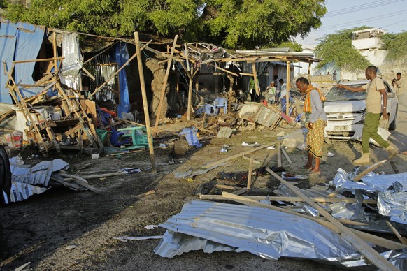 People stand near the wreckage of a car and kiosks after a bombing in Mogadishu, Somalia, Friday, Sept. 29, 2023. (AP Photo/Farah Abdi Warsameh)