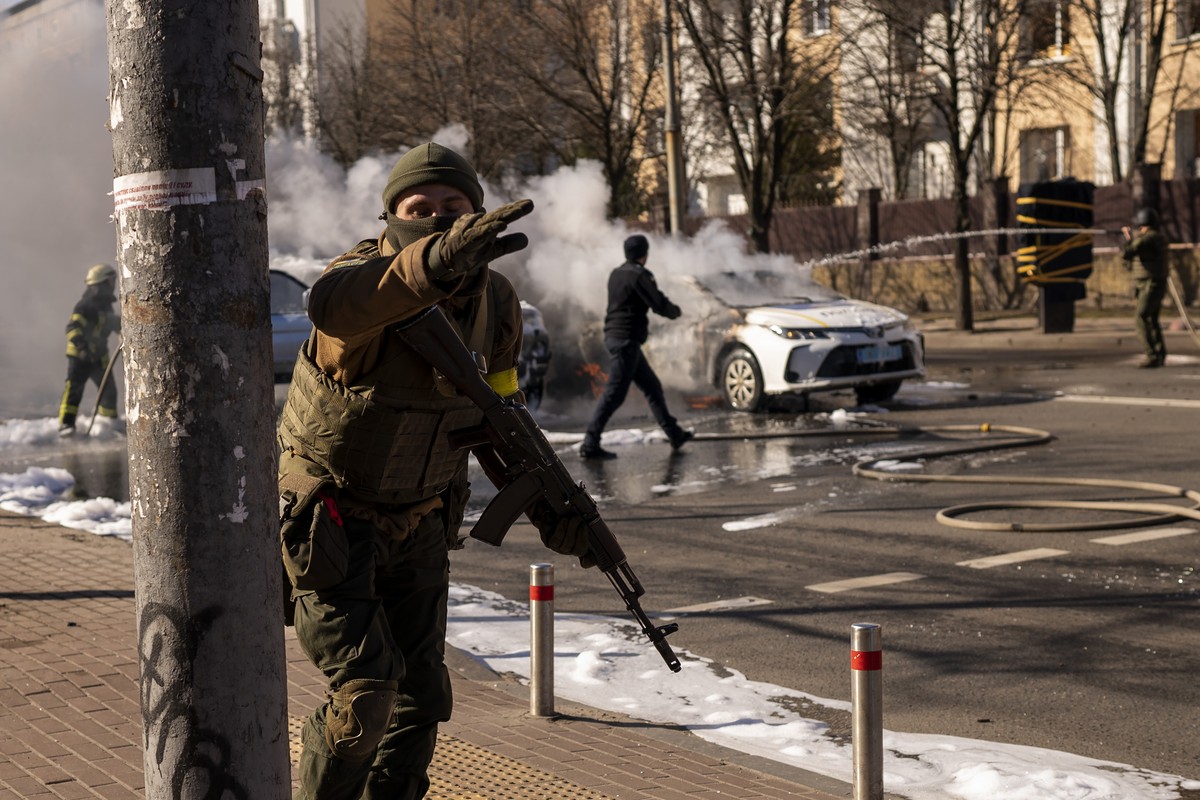 Ukrainian soldiers take positions outside a military facility as two cars burn, in a street in Kyiv, Ukraine, Saturday, Feb. 26, 2022. Russian troops stormed toward Ukraine's capital Saturday, an ...