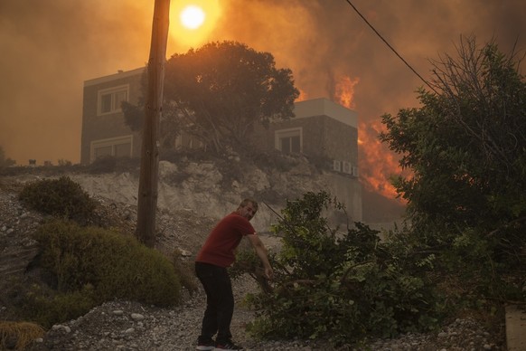 A local pulls a tree branch as a wildfire burns in Gennadi village, on the Aegean Sea island of Rhodes, southeastern Greece, on Tuesday, July 25, 2023. A firefighting plane has crashed in southern Gre ...