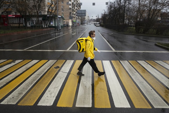 In this photo taken on Thursday, April 16, 2020, Russian businessman Sergey Nochovnyy wearing a face mask to protect against coronavirus crosses a road, on his way to pick up a food order to deliver,  ...