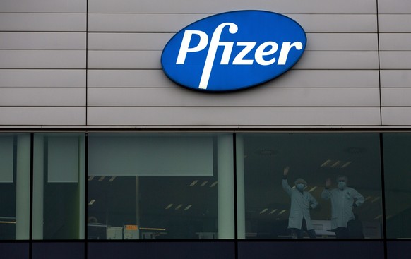 Two workers wave from a window at Pfizer Manufacturing in Puurs, Belgium, on Wednesday, Dec. 2, 2020. British officials authorized a COVID-19 vaccine for emergency use on Wednesday, greenlighting the  ...