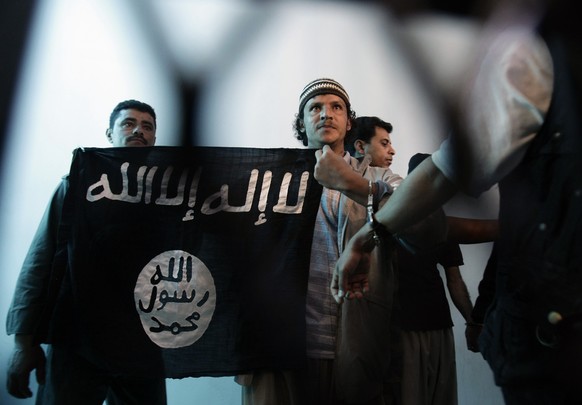 FILE - In this Tuesday, April 23, 2013 file photo, a suspected Yemeni al-Qaida militant, center, holds an Islamist banner as he stands behind bars during a court hearing in state security court in San ...