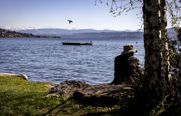 Eine Person sitzt bei sonnigem Wetter am Seeufer des Zuerichsees am Zuerichhorn, am Montag, 7. April 2025 in Zuerich. (KEYSTONE/Michael Buholzer)..