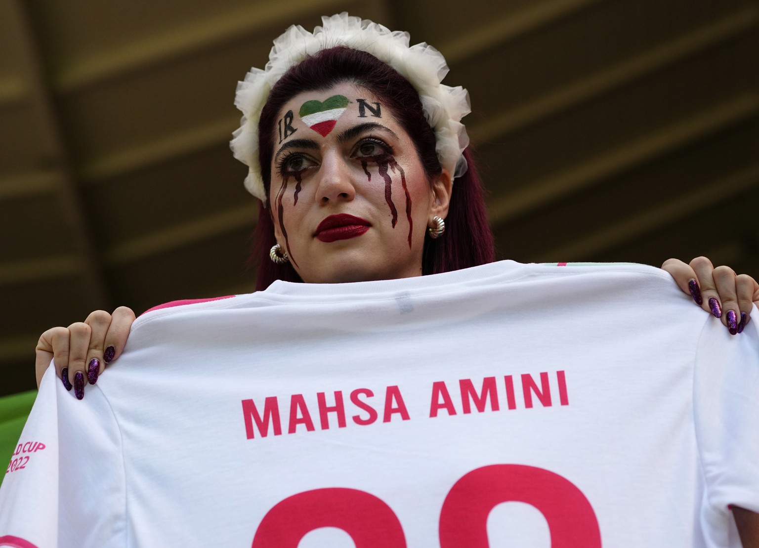 A fan painted her face holds a jersey with the name of Mahsa Amini, a woman who died while in police custody in Iran at the age of 22, ahead of the World Cup group B soccer match between Wales and Ira ...