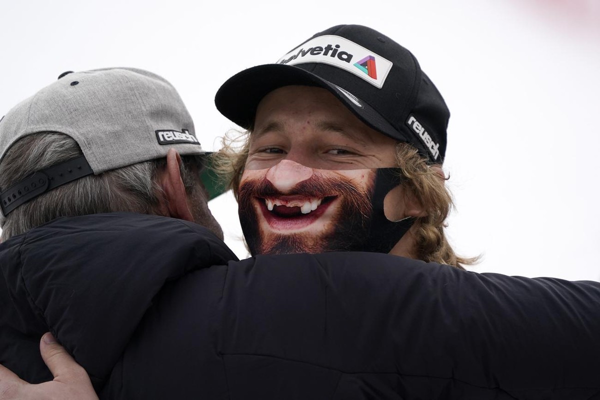 Switzerland's Marco Odermatt wears a face mask to curb the spread of COVID-19 as he is congratulated by teammates after winning an alpine ski, men's World Cup super G, in Saalbach-Hinterglem ...