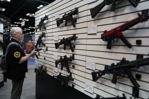 Kurt Adams examines a gun during the National Rifle Association Convention, Saturday, April 15, 2023, in Indianapolis.  (AP Photo/Darron Cummings)