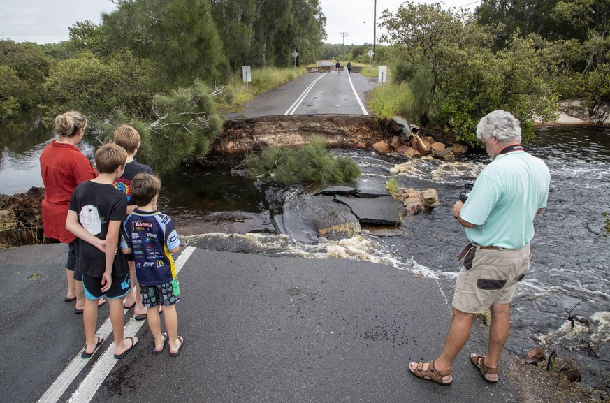 People stand at a washed out section of road at Port Stephens 200 kilometers (124 miles) north of Sydney, Australia, Saturday, March 20, 2021. People across New South Wales have been warned to expect ...