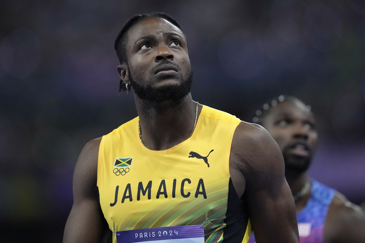 Kishane Thompson, of Jamaica, and Noah Lyles, of the United States, in the background, wait for the official results after finishing the men's 100 meters final at the 2024 Summer Olympics, Sunday ...