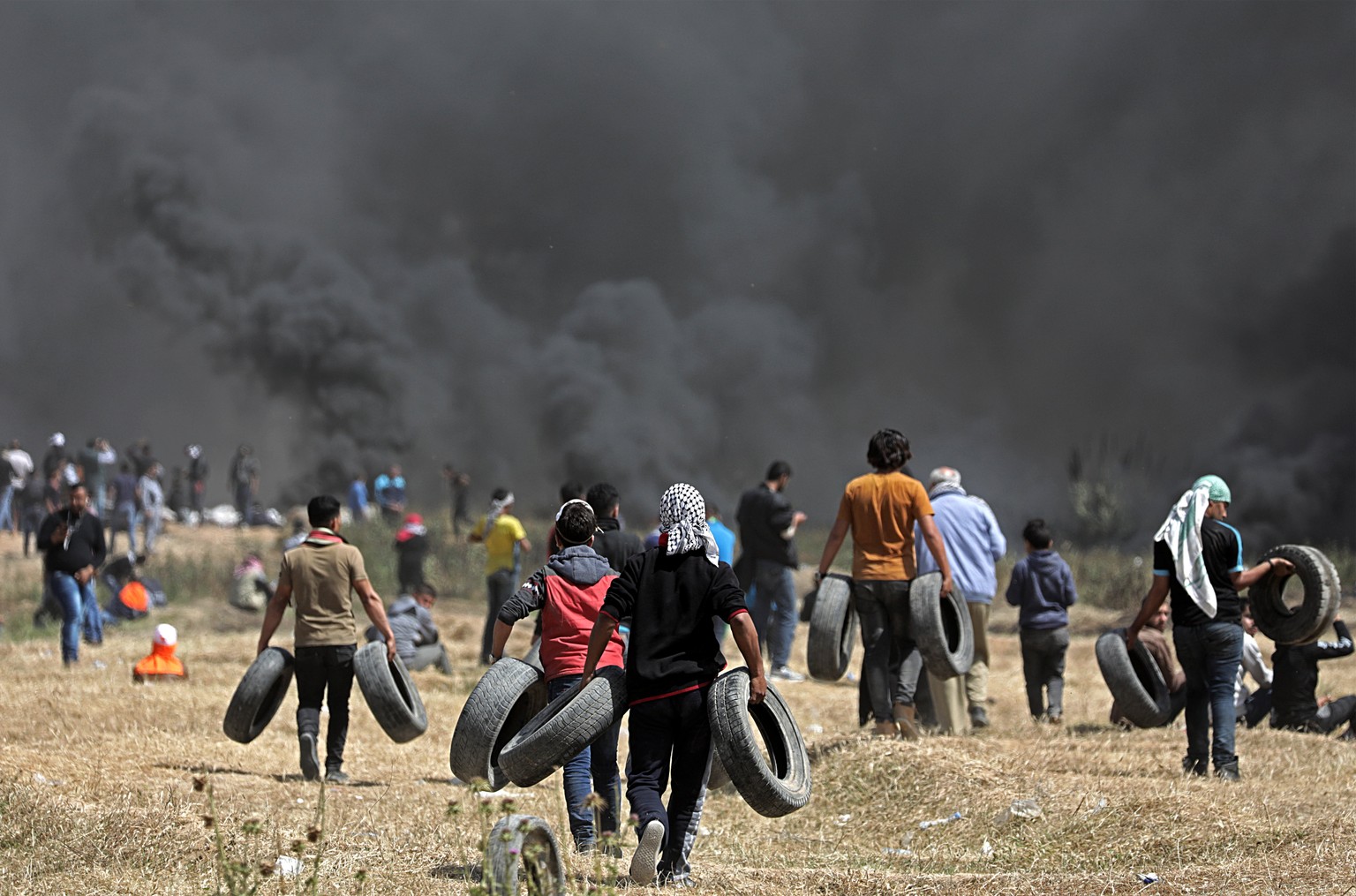 epa06649991 Protesters carry tires as other burn more tires to create a wall of smoke to act as cover for Palestinians protesters taking part during clashes with Israeli troops, near the border with I ...