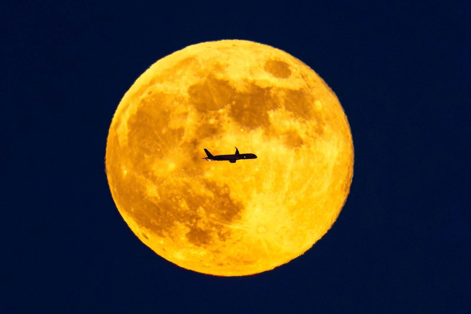 A planes passes across the full moon as it rises over London, seen from Sandown racecourse in Esher, England, Saturday, Jan. 3, 2026. (Steven Paston/PA via AP)