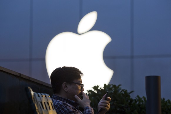 A man uses his mobile phone near a Apple store logo in Beijing, China, Friday, May 13, 2016. Apple Inc. has invested $1 billion in Chinese ride-hailing service Didi Chuxing, the main competitor in Chi ...