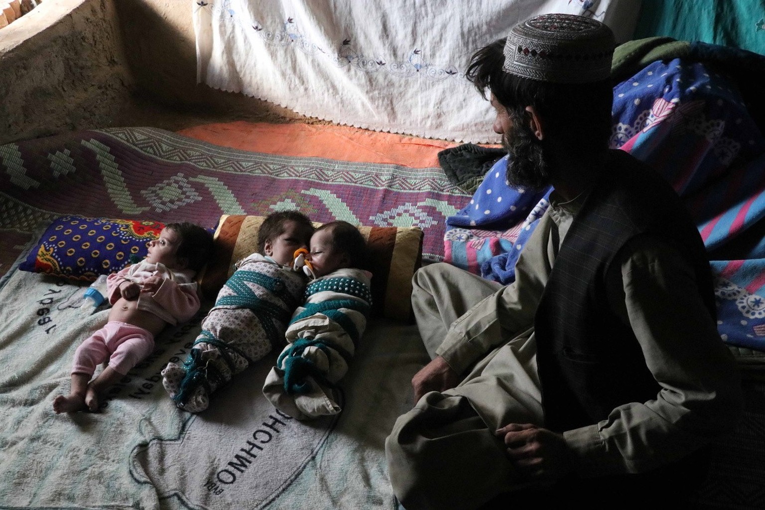 epa09625453 Ehsanullah, a father or newborn triplets sons sit next to his babies at his home in Kandahar, Afghanistan, 06 December 2021. Ehsanullahl said he was grateful to Allah for blessing him with ...
