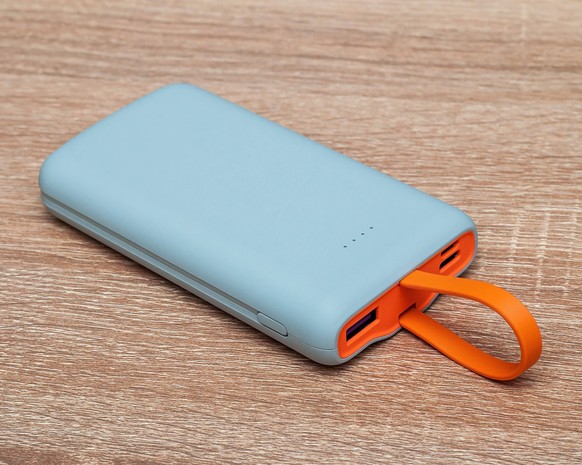 Ein modernes Gadget zum Aufladen von Geräten, eine Powerbank mit orangefarbenem USB-Griff auf einem hölzernen Hintergrund. Ein modernes Gadget zum Aufladen von Geräten, eine Powerbank mit orangefarben ...