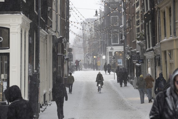 A woman rides her bicycle and others take a stroll in the center of Amsterdam, as snow and strong winds blanketed much of the Netherlands, Sunday, Feb. 7, 2021. (AP Photo/Peter Dejong)