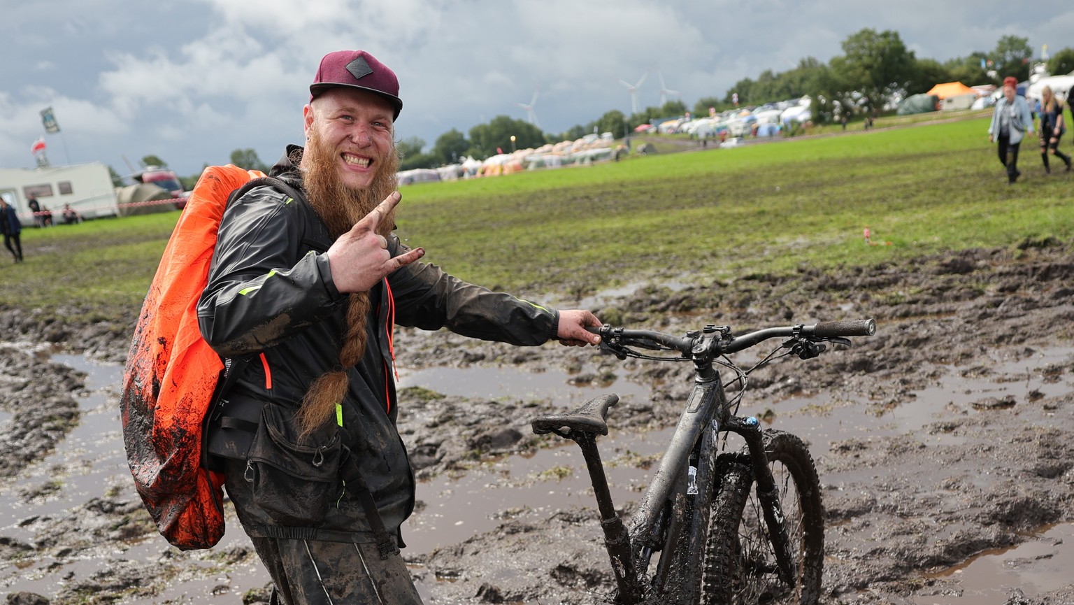 01.08.2023, Schleswig-Holstein, Wacken: Metal-Fan Lukas Litwin aus Bochum ist mit seinem E-Mountainbike auf dem schlammigen Festivalgel