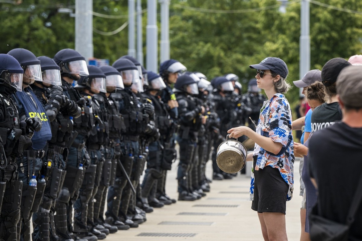 People protest in front of Swiss riot police at a public lecture by Women's rights activist "Posie Parker" (real name Kellie-Jay Keen), during a Let Women Speak rally on the place des N ...