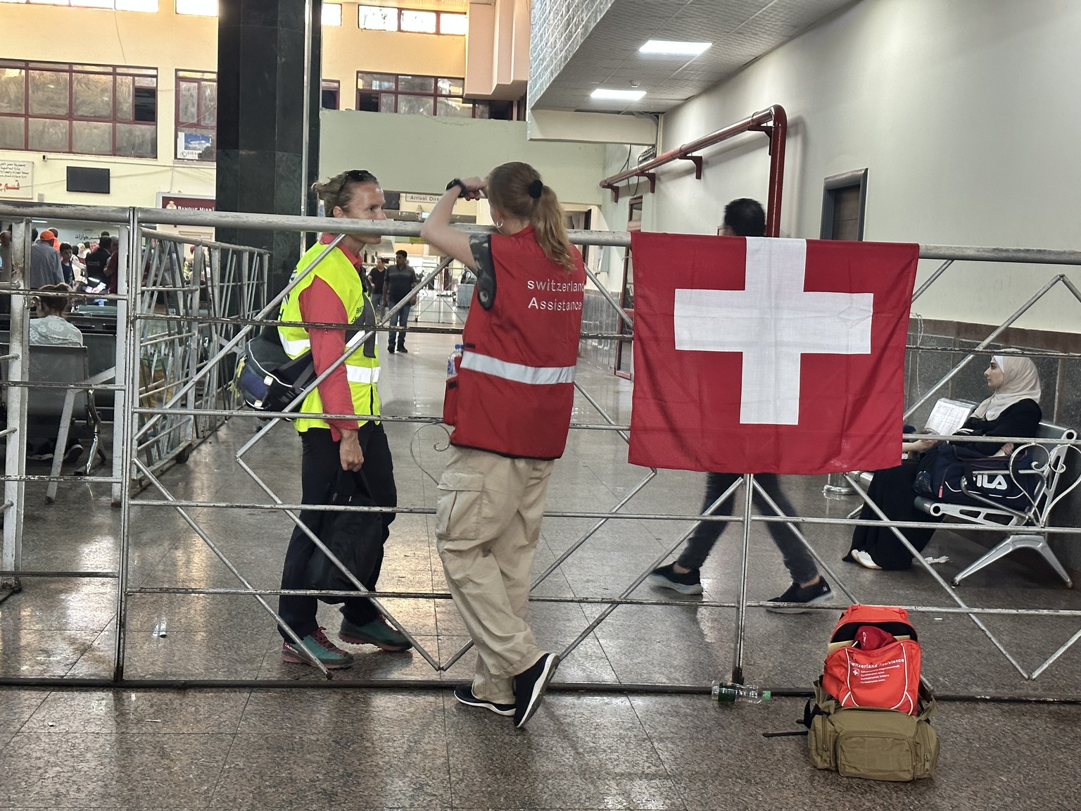 epa10954348 People stand next to a Swiss flag as they wait for the arrival of foreign nationals at the Egyptian side of the border after passing the Rafah border crossing between the Gaza Strip and Eg ...