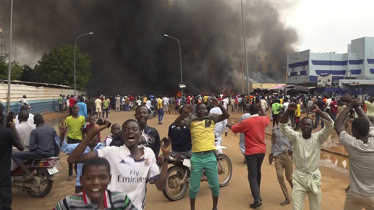 With the headquarters of the ruling party burning in the back, supporters of mutinous soldiers demonstrate in Niamey, Niger, Thursday, July 27 2023. Not everyone is hostile to last week's coup in ...