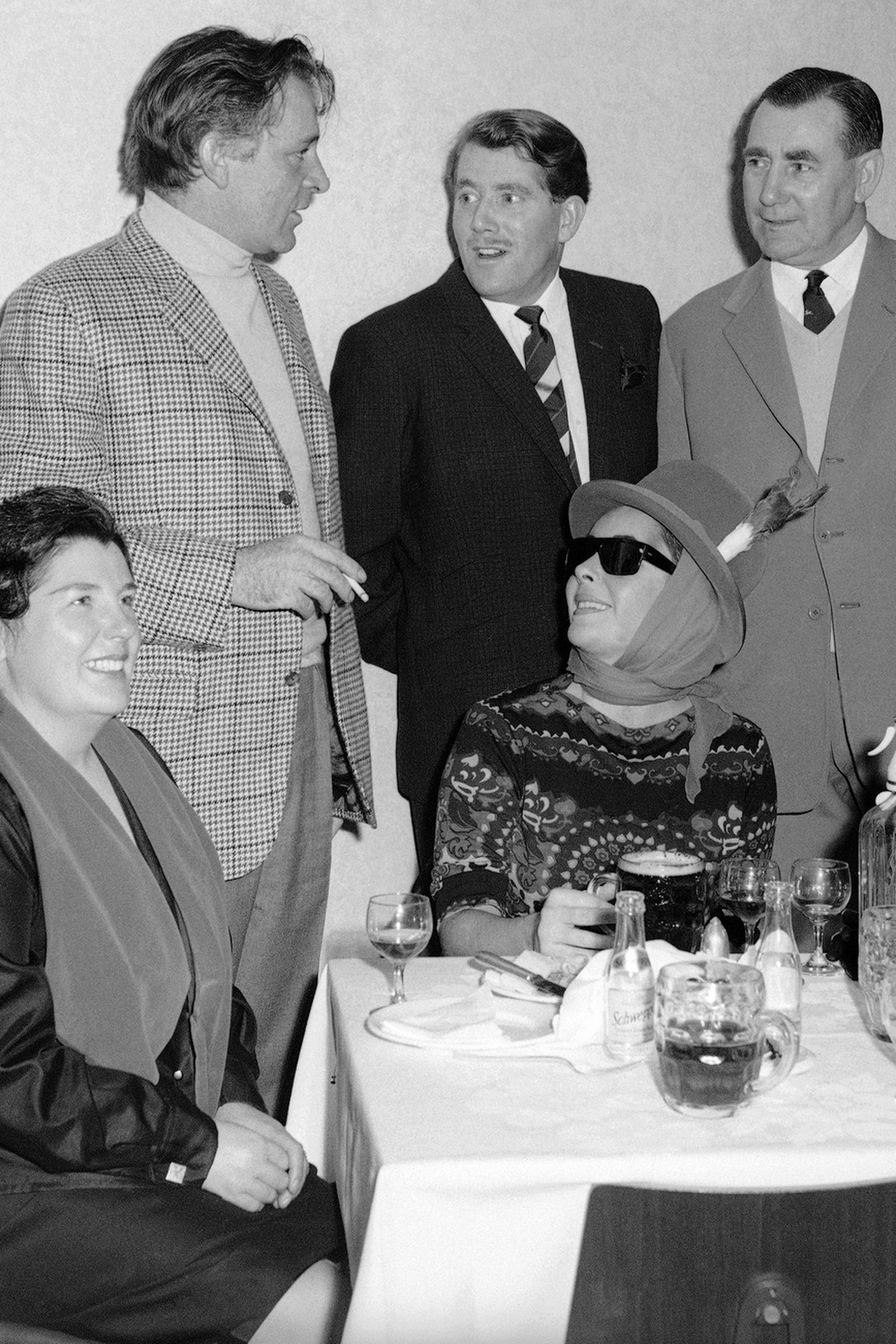 ritish-born American actress Elizabeth Taylor, dressed in a colorful sports outfit, looks up from her pint of beer as her husband, Welsh actor Richard Burton, talks to friends on Jan. 16, 1965 in Card ...