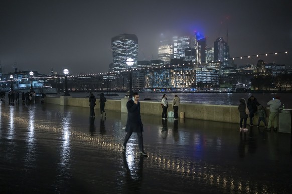 People walk along the bank of the River Thames with the skyline of the financial district in London, Wednesday, Jan. 25, 2023. (AP Photo/Kin Cheung)