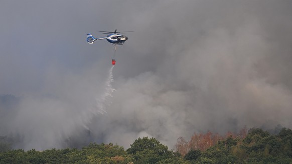 14.08.2026, Nordrhein-Westfalen, Hürtgenwald: Ein Polizeihubschrauber mit Löschwasser-Außenlastbehälter unterstützt die Löscharbeiten beim Waldbrand im Hürtgenwald. Mehrere Hundert Hektar Waldfläche s ...