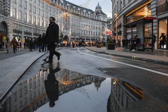 A man wears a face mask while he walks and is reflected into a puddle in Regent Street, ahead of the new Tier-4 restriction measures, in London, Saturday, Dec. 19, 2020. Britain's Prime Minister Boris Johnson says Christmas gatherings cannot go ahead and non-essential shops must close in London and much of southern England as he imposed a new, higher level of coronavirus restrictions to curb rapidly spreading infections.(AP Photo/Alberto Pezzali)