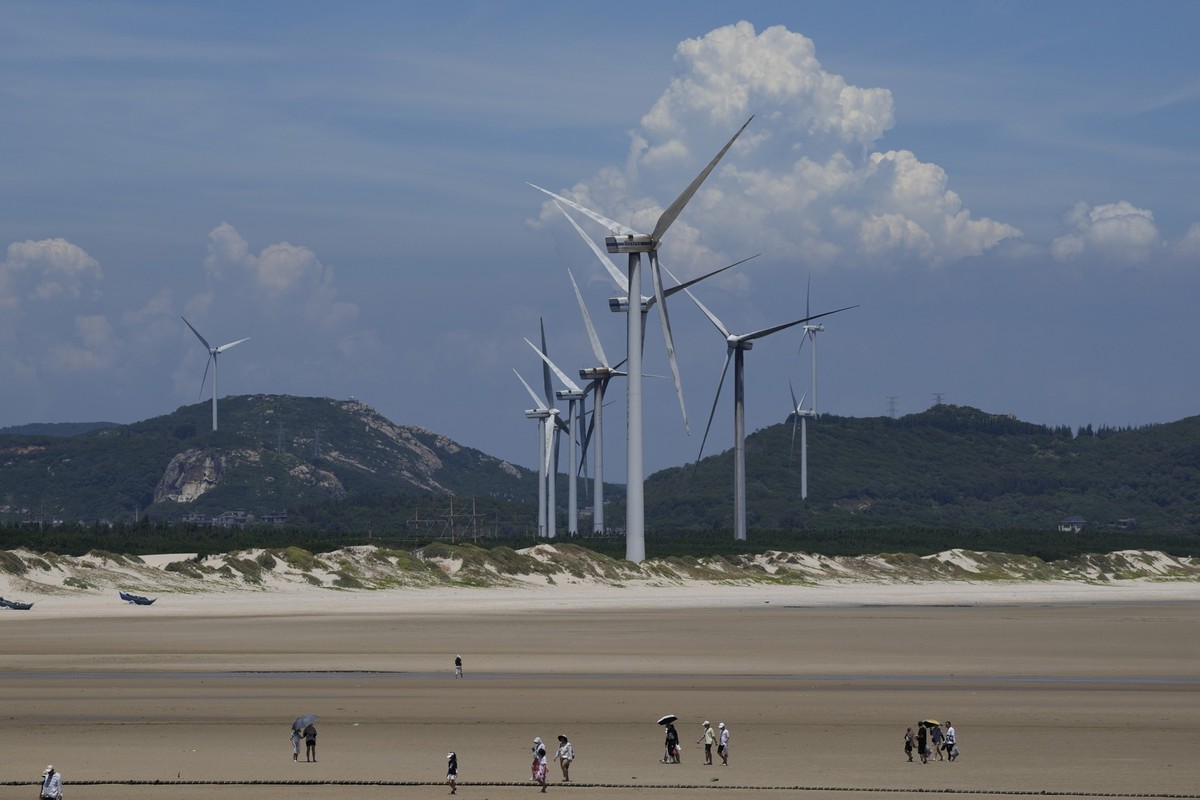 FILE - Beachgoers walk near wind turbines along the coast of Pingtan in Southern China's Fujian province on Aug. 6, 2022. The majority of developing nations are set to miss out on the economic be ...