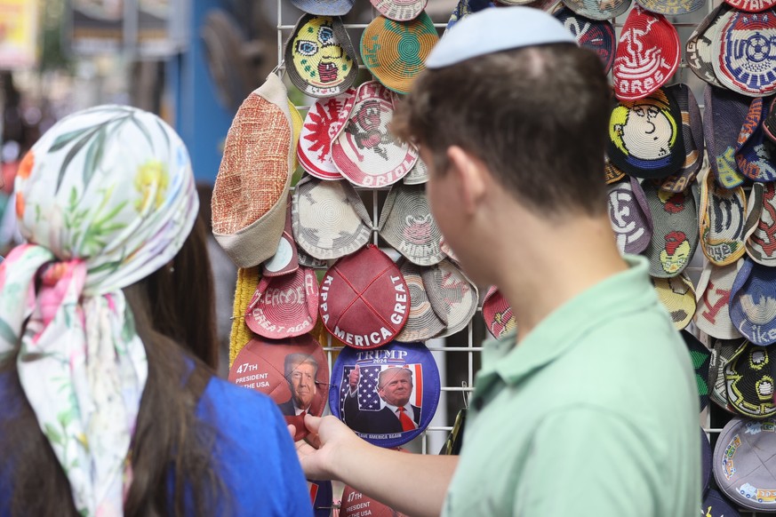 epa12444450 People walk past a shop selling Jewish skullcaps, known as a kippah (Hebrew) or yarmulke (Yiddish), featuring an image of U.S. President Donald Trump at a market in Jerusalem, Israel, 10 O ...