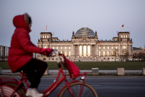 A woman rides past the Reichstag building, the seat of the German Bundestag in Berlin, Monday, March 23, 2020. Despite the COVID-19 crisis, the Bundestag wants to meet for a session on Wednesday. In order to slow down the spread of the coronavirus, the federal government has considerably restricted public life. (Carsten Koall/dpa via AP)