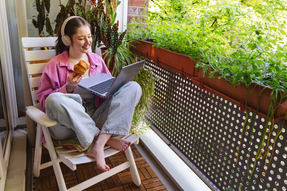 Woman eats croissant while working on laptop on sunny balcony model released, Symbolfoto property released, IHF02919