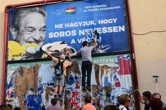 Activists from the Egyutt (Together) party tear down an ad by the Hungarian government against George Soros, in Budapest, Wednesday, July 12, 2017. The Hungarian government said Wednesday it will soon ...