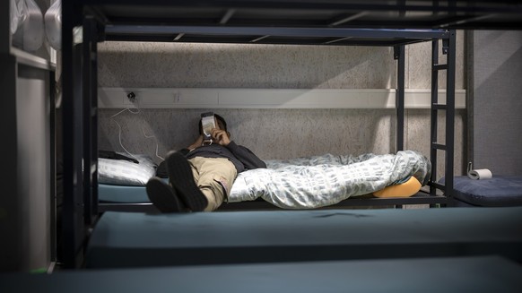 Ein Mann benutzt sein Mobiltelefon waehrend er in einem Schlafsaal auf einem Bett liegt, aufgenommen waehrend eines Medienrundgans im Bundesasylzentrum Zuerich, am Donnerstag, 27. Oktober 2022 in Zuer ...