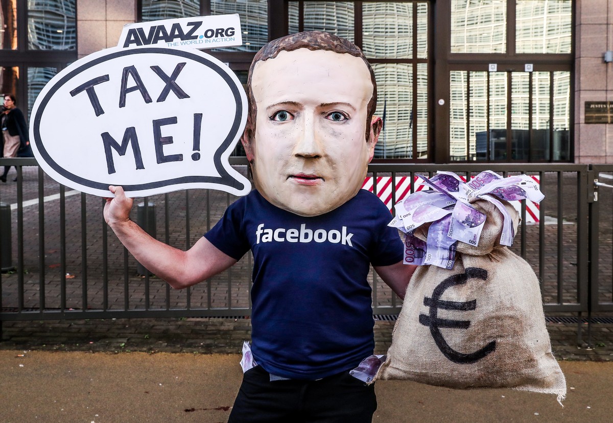 epa07207687 An activist wearing a mask depicting Facebook's CEO Mark Zuckerberg holds a banner reading 'Tax me' at the start of an European Union Finance Ministers Meeting in front of t ...