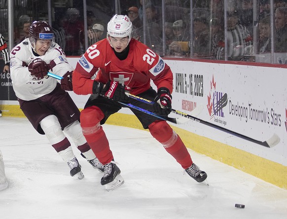 Latvia's Roberts Cjunskis hooks Switzerland's Lian Bichsel during the first period of an IIHF World Junior Hockey Championship hockey game against Switzerland in Moncton, New Brunswick, on T ...