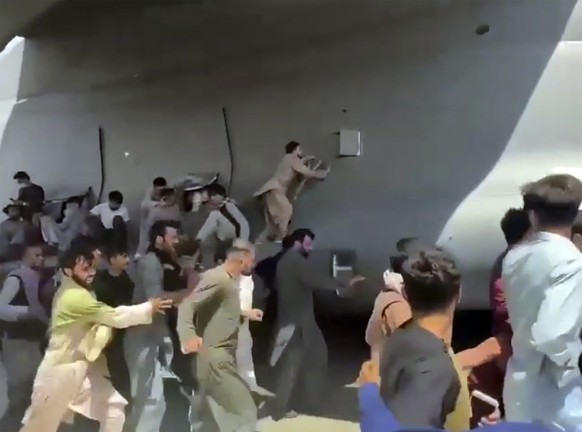 Hundreds of people run alongside a U.S. Air Force C-17 transport plane, some climbing on the plane, as it moves down a runway of the international airport, in Kabul, Afghanistan, Monday, Aug.16. 2021. ...