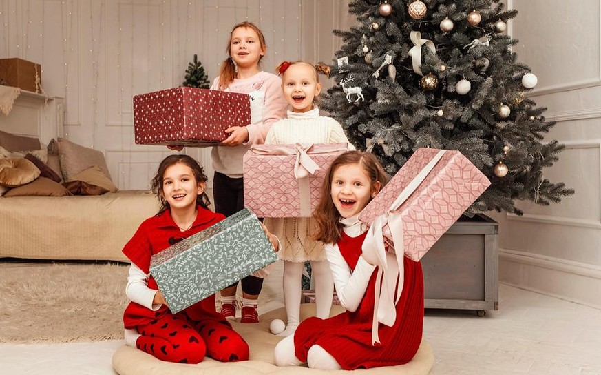 Christmas girls with gifts present boxes. Christmas party four girls hold boxes of gifts and rejoice. Children sit by the Christmas tree and unpack gifts