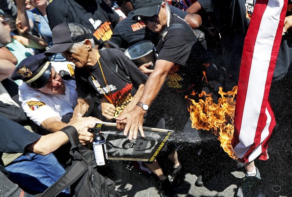 A law enforcement officer tries extinguish a burning American flag, Wednesday, July 20, 2016, in Cleveland, during the third day of the Republican convention. (AP Photo/John Minchillo)