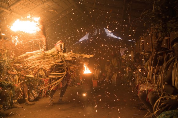 NGOUNIé PROVINCE, GABON - 2024/08/17: Participants in a Bwiti ceremony, dressed in ritual attire made from dried palm leaves, dance with lit torches inside a small temple. Bwiti is an animistic practi ...