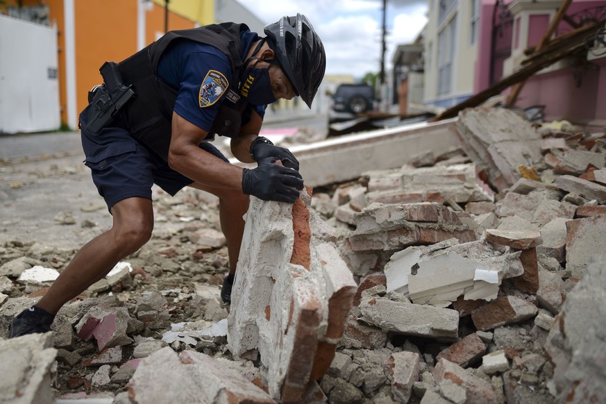 A police officer, wearing s protective face mask as a precaution against the spread of the new coronavirus, removes debris caused by a 5.4-magnitude earthquake, in Ponce, Puerto Rico, Saturday, May 2, ...