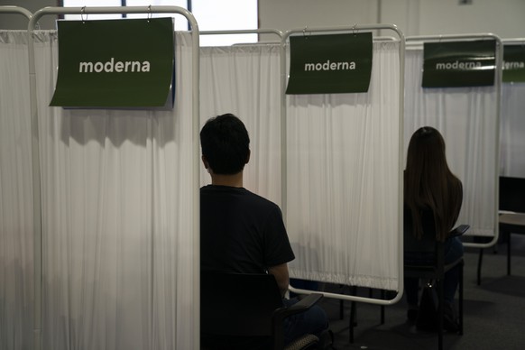 Two people wait to receive the Moderna COVID-19 vaccine at Providence Edwards Lifesciences vaccination site in Santa Ana, Calif., Friday, May 21, 2021. California no longer will require social distanc ...