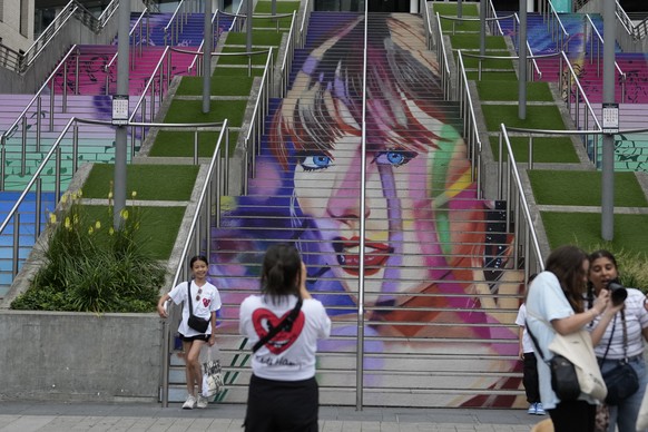 Fans pose by a Taylor Swift portrait painted on a stairway at Wembley Stadium in London, Wednesday, Aug. 14, 2024, ahead of a series of Taylor Swift concerts starting Thursday. (AP Photo/Alastair Gran ...