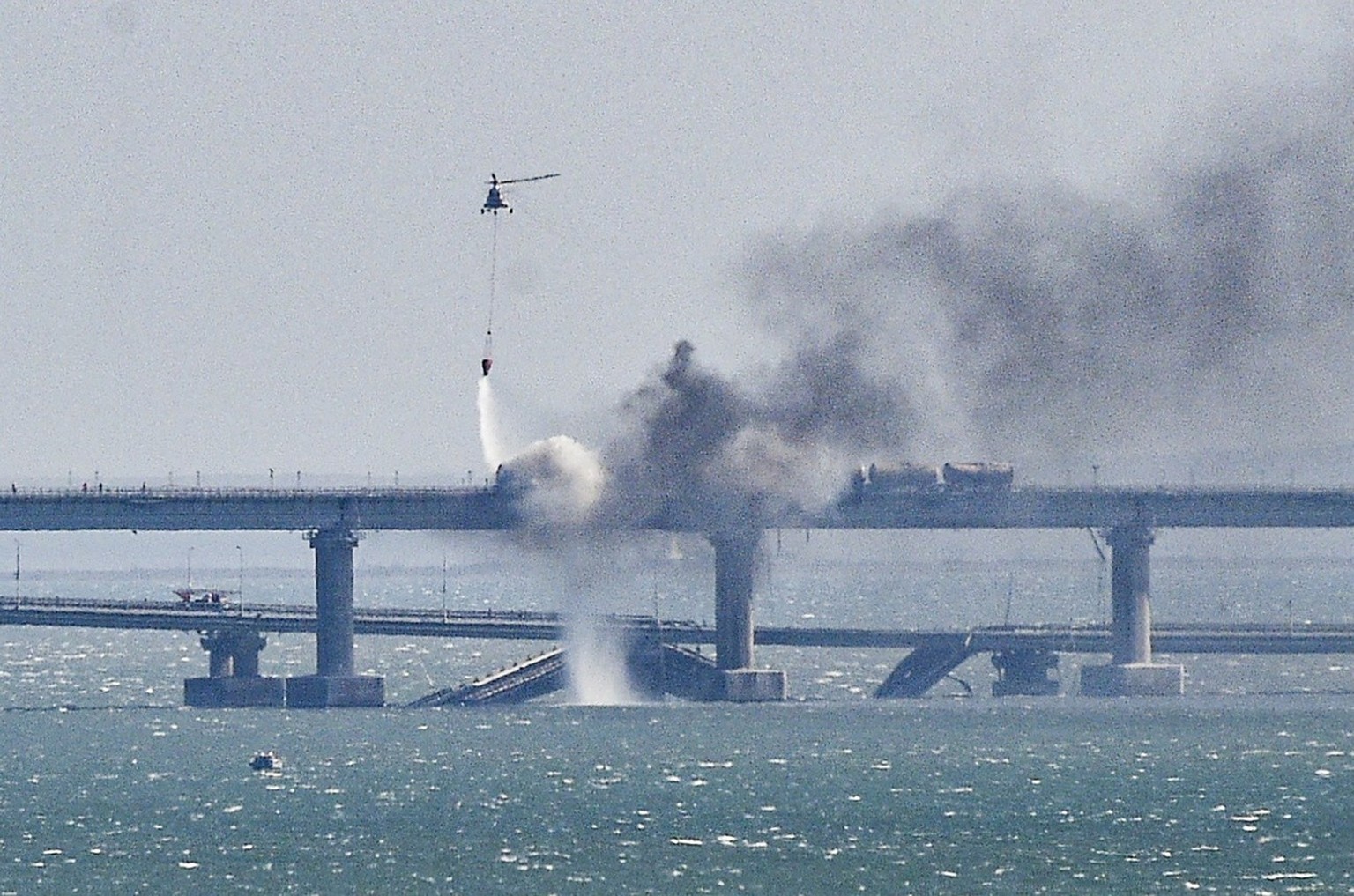epa10364888 A firefighter helicopter pours water on fire on a collapsed part of the Kerch Strait bridge in Crimea, 08 October 2022. EPA/STRINGER