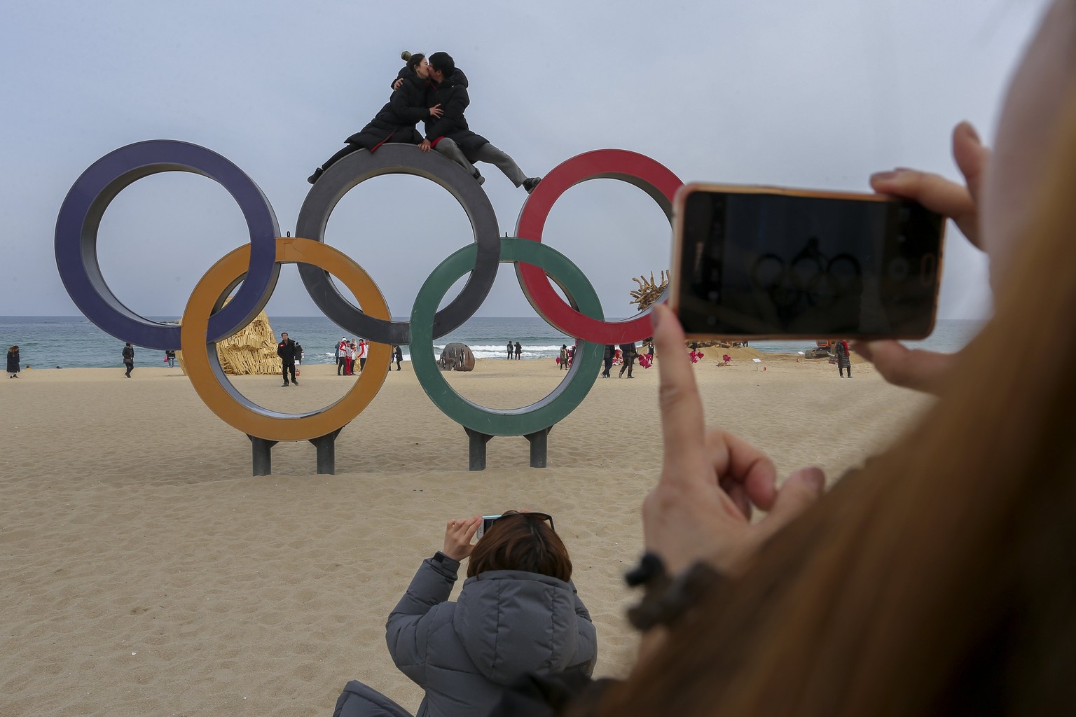 epa06541997 Tourists posing for photos sit on top of the Olympic rings at Gyeongpo beach near the Olympic village in Gangneung, South Korea, 19 February 2018. EPA/VALDRIN XHEMAJ