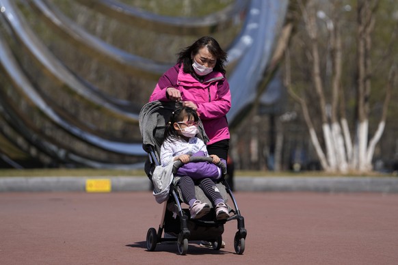 A woman wearing a face mask to help protect from the coronavirus brings a masked child visit to a park, Sunday, April 3, 2022, in Beijing. COVID-19 cases in China's largest city of Shanghai are still rising as millions remain isolated at home under a sweeping lockdown. (AP Photo/Andy Wong)